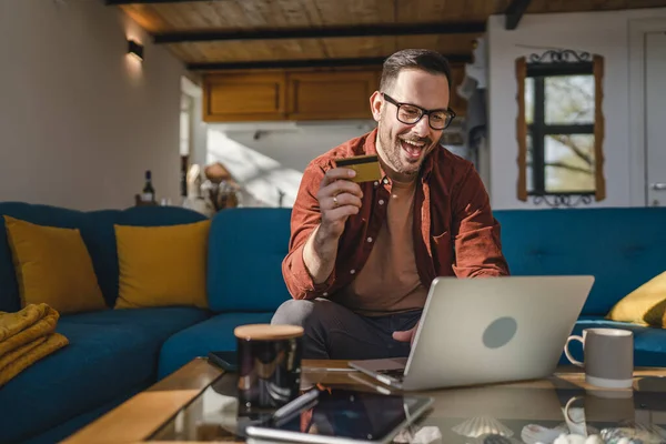 stock image One man adult mature caucasian male sit at home happy smile with laptop computer hold bank credit card online shopping buy on internet concept real people copy space e-commerce e-banking service