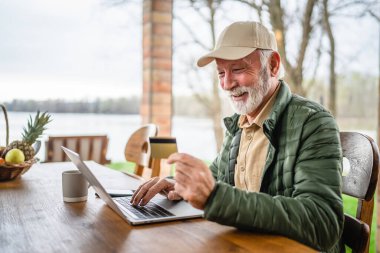 Sakallı, kıdemli, beyaz bir erkek bütün gün dışarıda dizüstü bilgisayarla alışveriş yapıyor. Bir şeyler alıyor, kredi kartı kullanıyor. Emekliliğinin tadını çıkarıyor.