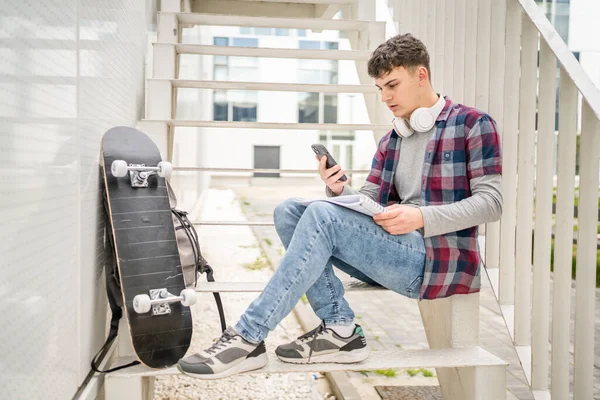 stock image One Young man teenager caucasian student with books read study at campus in day sit on staircase education concept copy space use smartphone mobile phone for online text or sms app social network