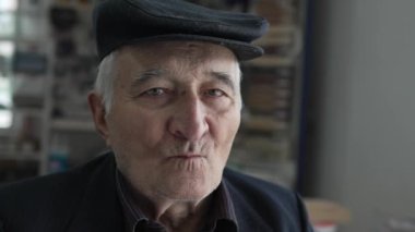 Kafkasyalı yaşlı bir adamın portresi. Büyükbaba içeride oturuyor. Şapka takıyor ve kameraya bakıyor.