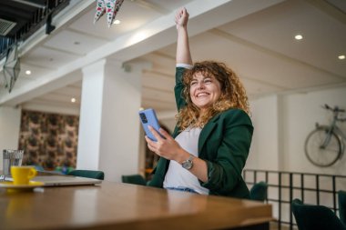 Kafe 'de oturan yetişkin bir kadın internet gezmek ya da mesaj atmak için akıllı telefon kullanır. Mutlu bir gülümseme, güler yüzlü gerçek bir insana iyi haberler verir ya da ödeme alanının kopyalarını verir.