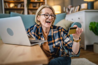 Yetişkin bir yaşlı kadın büyükanne evde oturup online alışveriş siteleri için kredi kartı ya da banka kartı kullanıyor. Bir şeyler satın alıyor. Dijital tablet kullanıyor. Gerçek insanlar yer kopyalıyor.