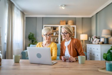 İki olgun yaşlı kadın büyükanne kadın evde oturup online alışveriş siteleri için kredi kartı ya da banka kartı kullanıyor. Bir şeyler satın alıyorlar. Dijital tablet kullanıyorlar. Gerçek insanlar yer kopyalıyor.