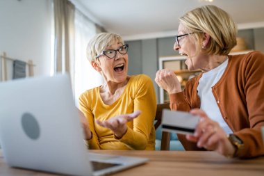 İki olgun yaşlı kadın büyükanne kadın evde oturup online alışveriş siteleri için kredi kartı ya da banka kartı kullanıyor. Bir şeyler satın alıyorlar. Dijital tablet kullanıyorlar. Gerçek insanlar yer kopyalıyor.