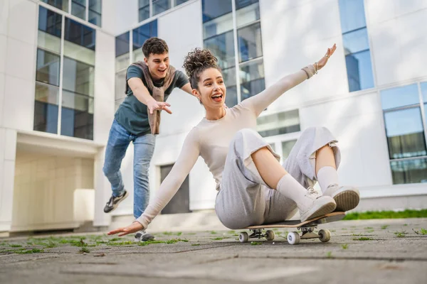 年轻男女青少年情侣哥妹俩在滑板上玩得开心 在现代建筑旁推挤着骑着快乐的微笑真实的人家庭爱的概念复制的空间 — 图库照片