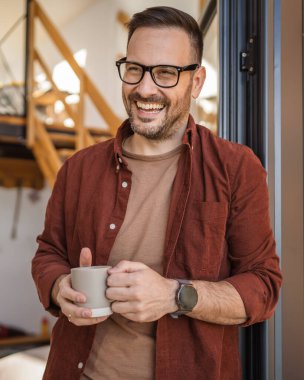 Beyaz erkek, 40 yaşında, balkonda elinde çay ya da kahveyle dikilen bir gömlek giyiyor. Günlük rutininin huzurlu bir anının tadını çıkarıyor. Ya da tatil fotokopi odasında.