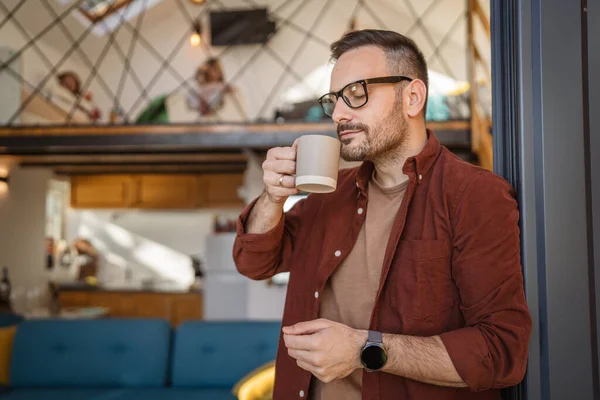 40岁的男子穿着衬衫站在阳台上 高兴地捧着一杯茶或咖啡 他正在日常的早晨活动中或在度假时享受着片刻的宁静 — 图库照片
