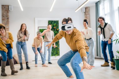 Yetişkin bir beyaz erkek, bir grup erkek ve kadın arkadaşın önünde sanal gerçeklik cihazının keyfini çıkarıyor. Takım oluşturma semineri sırasında birlikte eğleniyorlar. Gerçek insanlar parlak filtreler.