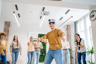 Yetişkin bir beyaz erkek, bir grup erkek ve kadın arkadaşın önünde sanal gerçeklik cihazının keyfini çıkarıyor. Takım oluşturma semineri sırasında birlikte eğleniyorlar. Gerçek insanlar parlak filtreler.