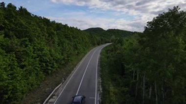Sırbistan 'da yeşil ve manzara taşımacılığı ve seyahat konseptiyle çevrili dolambaçlı yol boyunca giden bahar aracı otomobili sırasında, bir dağ sırasındaki eğimli asfalt bir yolun hava aracı görüntüleri