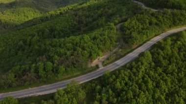 Sırbistan 'da yeşil ve manzara taşımacılığı ve seyahat konseptiyle çevrili dolambaçlı yol boyunca giden bahar aracı otomobili sırasında, bir dağ sırasındaki eğimli asfalt bir yolun hava aracı görüntüleri