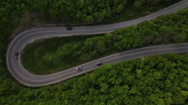 Sırbistan 'da yeşil ve manzara taşımacılığı ve seyahat konseptiyle çevrili dolambaçlı yol boyunca giden bahar aracı otomobili sırasında, bir dağ sırasındaki eğimli asfalt bir yolun hava aracı görüntüleri