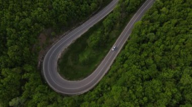 Sırbistan 'da yeşil ve manzara taşımacılığı ve seyahat konseptiyle çevrili dolambaçlı yol boyunca giden bahar aracı otomobili sırasında, bir dağ sırasındaki eğimli asfalt bir yolun hava aracı görüntüleri