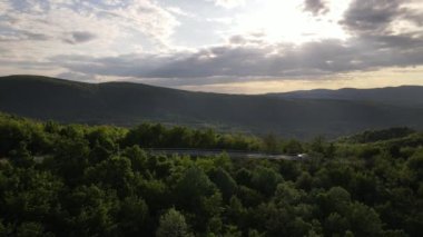 Sırbistan 'da yeşil ve manzara taşımacılığı ve seyahat konseptiyle çevrili dolambaçlı yol boyunca giden bahar aracı otomobili sırasında, bir dağ sırasındaki eğimli asfalt bir yolun hava aracı görüntüleri