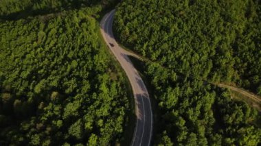 Sırbistan 'da yeşil ve manzara taşımacılığı ve seyahat konseptiyle çevrili dolambaçlı yol boyunca giden bahar aracı otomobili sırasında, bir dağ sırasındaki eğimli asfalt bir yolun hava aracı görüntüleri