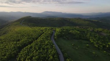 Sırbistan 'da yeşil ve manzara taşımacılığı ve seyahat konseptiyle çevrili dolambaçlı yol boyunca giden bahar aracı otomobili sırasında, bir dağ sırasındaki eğimli asfalt bir yolun hava aracı görüntüleri