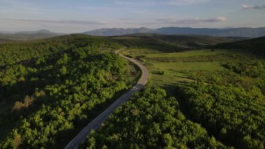 Sırbistan 'da yeşil ve manzara taşımacılığı ve seyahat konseptiyle çevrili dolambaçlı yol boyunca giden bahar aracı otomobili sırasında, bir dağ sırasındaki eğimli asfalt bir yolun hava aracı görüntüleri