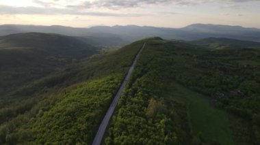 Sırbistan 'da yeşil ve manzara taşımacılığı ve seyahat konseptiyle çevrili dolambaçlı yol boyunca giden bahar aracı otomobili sırasında, bir dağ sırasındaki eğimli asfalt bir yolun hava aracı görüntüleri