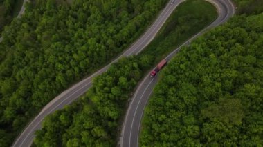 Sırbistan 'da yeşil ve manzara taşımacılığı ve seyahat konseptiyle çevrili dolambaçlı yol boyunca giden bahar aracı kamyonları sırasında bir dağ sırasındaki eğri asfalt bir yolun hava aracı görüntüleri