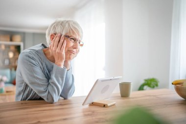 Yetişkin bir yaşlı kadın büyükanne evde oturup online alışveriş siteleri için kredi kartı ya da banka kartı kullanıyor. Gerçek insanların hayal kırıklığını kopyaladığı şeyler alıyor.