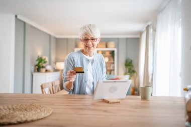 Yetişkin bir yaşlı kadın büyükanne evde oturup online alışveriş siteleri için kredi kartı ya da banka kartı kullanıyor ve gerçek insanların yer kopyaladığı şeyleri alıyor.