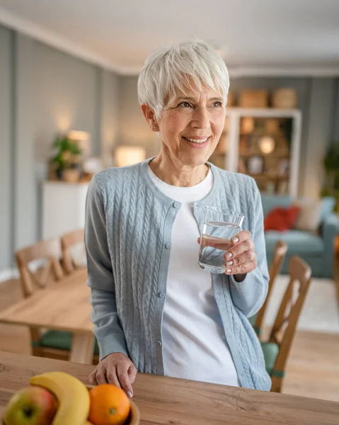 stock image Close up portrait of one senior woman with short hair happy smile positive emotion copy space standing at home indoor gray white hair hold glass of water