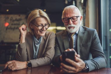 Takım elbiseli kıdemli bir adam ve iş ortağı olarak olgun sarışın bir kadın koca ve eş ya da baba kız konuşmaları ellerinde akıllı telefonlarla internet paylaşımı fikirleri kopyalayarak.