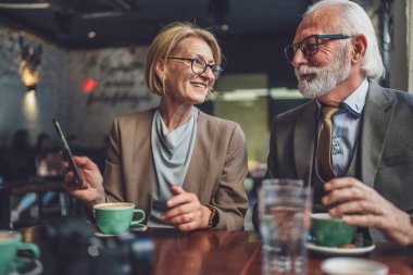 Takım elbiseli kıdemli bir adam ve iş ortağı olarak olgun sarışın bir kadın koca ve eş ya da baba kız konuşmaları ellerinde akıllı telefonlarla internet paylaşımı fikirleri kopyalayarak.