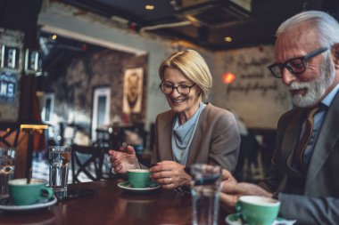 Seçkin sakallı kıdemli bir adam ve olgun sarışın bir kadın karı koca iş ortağı arkadaşlar ya da baba-kız, kahvede birbirlerine eşlik ederken mutlu olurlar gülümsemeleri olan akıllı telefonları kullanın.
