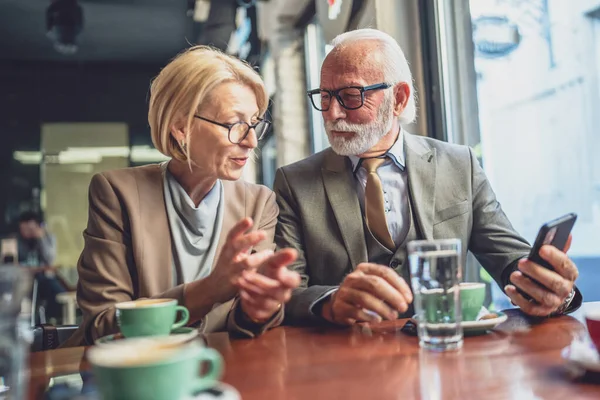 senior man with a distinguished beard and a mature blonde woman whether as husband and wife business partners or friends share a joyful moment at a cafe look at photos or connect with others