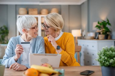 İki olgun yaşlı kadın büyükanne kız kardeş ya da arkadaş evlerinde oturup dijital tabletteki internet mağazaları için kredi kartı kullanıyorlar. İndirim indirimleri yapıyorlar.