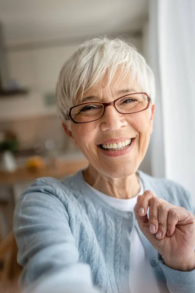 Close up portrait of one senior woman with short hair happy smile positive emotion copy space standing at home indoor gray white hair self portrait selfie or video call