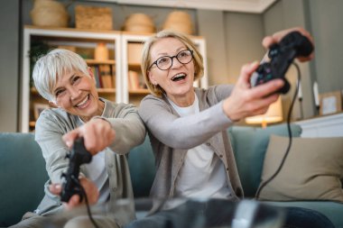 İki son sınıf beyaz kadın arkadaş ya da kız kardeş mutlu yaşlı kardeşler oyun konsolu oyunu oynayan emekli oyun konsolu kullanan evde otururken gerçek insanların gerçek eğlence konsepti olan uzay kopyası.