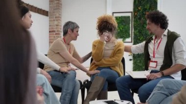 Bir grup insan, iki terapist ve merkezde bir kadınla bir çemberin içinde oturuyor ve ona duygusal destek sağlıyorlar.