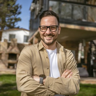 Bir modern yetişkin beyaz erkek portresi sakallı ve gözlüklü erkek evinin önünde duruyor. Mutlu, kendinden emin fotokopi odası.