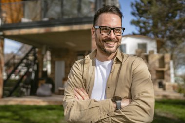 Bir modern yetişkin beyaz erkek portresi sakallı ve gözlüklü erkek evinin önünde duruyor. Mutlu, kendinden emin fotokopi odası.