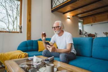 Son sınıflardan biri elinde ilaç ya da takviye ilaç şişesiyle kanepede oturuyor. Akıllı telefon, ilaç tableti, ağrı kesici ya da ilaç almaya hazır vitamin talimatları okuyor.