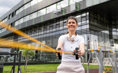 Bir kadın olgun ya da yaşlı, kauçuk elastik direnç bantlı beyaz kadın eğitimi. Açık spor salonunun spor salonundaki tüplerde. Sağlıklı yaşam tarzı konsepti.