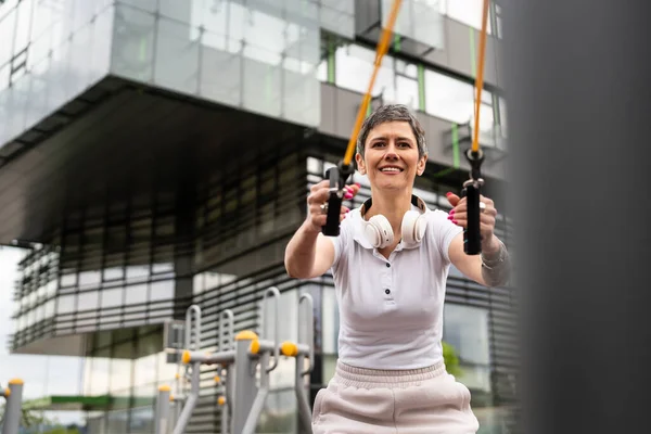 Bir kadın olgun ya da yaşlı, kauçuk elastik direnç bantlı beyaz kadın eğitimi. Açık spor salonunun spor salonundaki tüplerde. Sağlıklı yaşam tarzı konsepti.