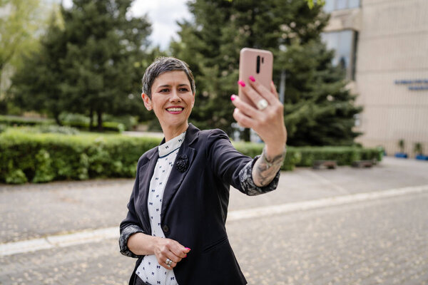 One woman mature or senior caucasian female standing outdoor alone taking selfie photos or making a video call happy smile confident real people modern lifestyle copy space