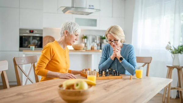 二人のシニア熟女白人女性の友人や姉妹遊びレジャーチェスボードゲーム自宅で楽しい時間を過ごしています一緒に家で明るい写真のコピースペース — ストック写真