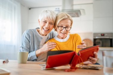 Yetişkin kadın arkadaşlar ya da kız kardeşler aile fotoğraflarına bakıyor. İki beyaz kadın evde oturup gülümserken gerçek insanlar uzayı kopyalıyor.