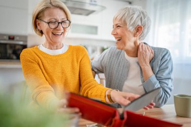 Yetişkin kadın arkadaşlar ya da kız kardeşler aile fotoğraflarına bakıyor. İki beyaz kadın evde oturup gülümserken gerçek insanlar uzayı kopyalıyor.