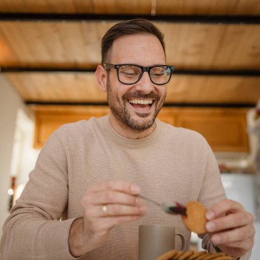 Yetişkin bir beyaz erkek, evde bir masaya oturup kahvaltıya hazırlanan reçel ve bisküvinin üzerine oturur. Ev ortamında rahatça atıştırır. Gerçek insan, günlük uzay rutinini taklit eder.
