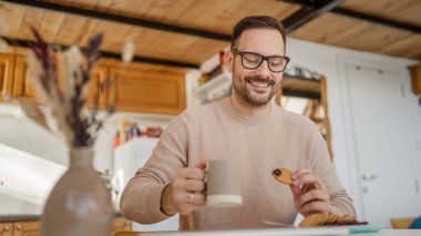 Yetişkin bir beyaz erkek, evde bir masaya oturup kahvaltıya hazırlanan reçel ve bisküvinin üzerine oturur. Ev ortamında rahatça atıştırır. Gerçek insan, günlük uzay rutinini taklit eder.