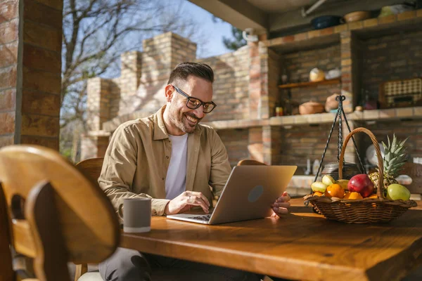 一位男子孤身一人坐在阳台上 身穿衬衫 坐在笔记本电脑上 心情愉快地微笑着 自信地把成功的理念复制了出来 — 图库照片