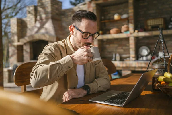 一位男子孤身一人坐在阳台上 身穿衬衫 坐在笔记本电脑上 心情愉快地微笑着 自信地把成功的理念复制了出来 — 图库照片