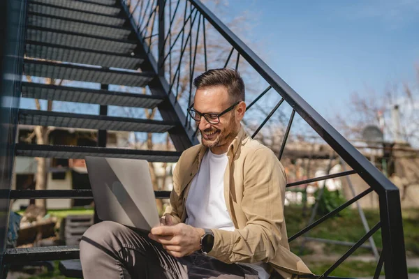 一名男子坐在楼梯上 独自坐在家里 穿着衬衫 在笔记本电脑上工作 在遥远的快乐微笑中 自信的成功理念复制了空间 — 图库照片