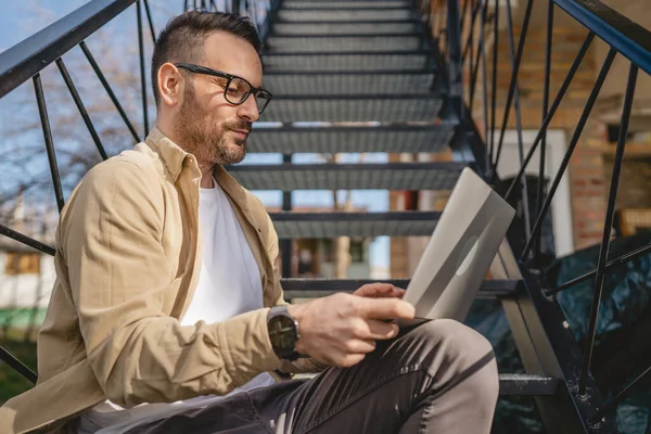 一名男子坐在楼梯上 独自坐在家里 穿着衬衫 在笔记本电脑上工作 在遥远的快乐微笑中 自信的成功理念复制了空间 — 图库照片