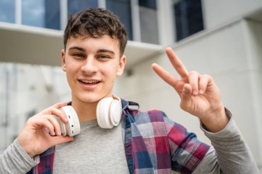 Genç, yetişkin, beyaz bir genç, dışarıda durup fotoğraf çekiyor. Kameraya bakıyor. Kendine güveni tamdır.